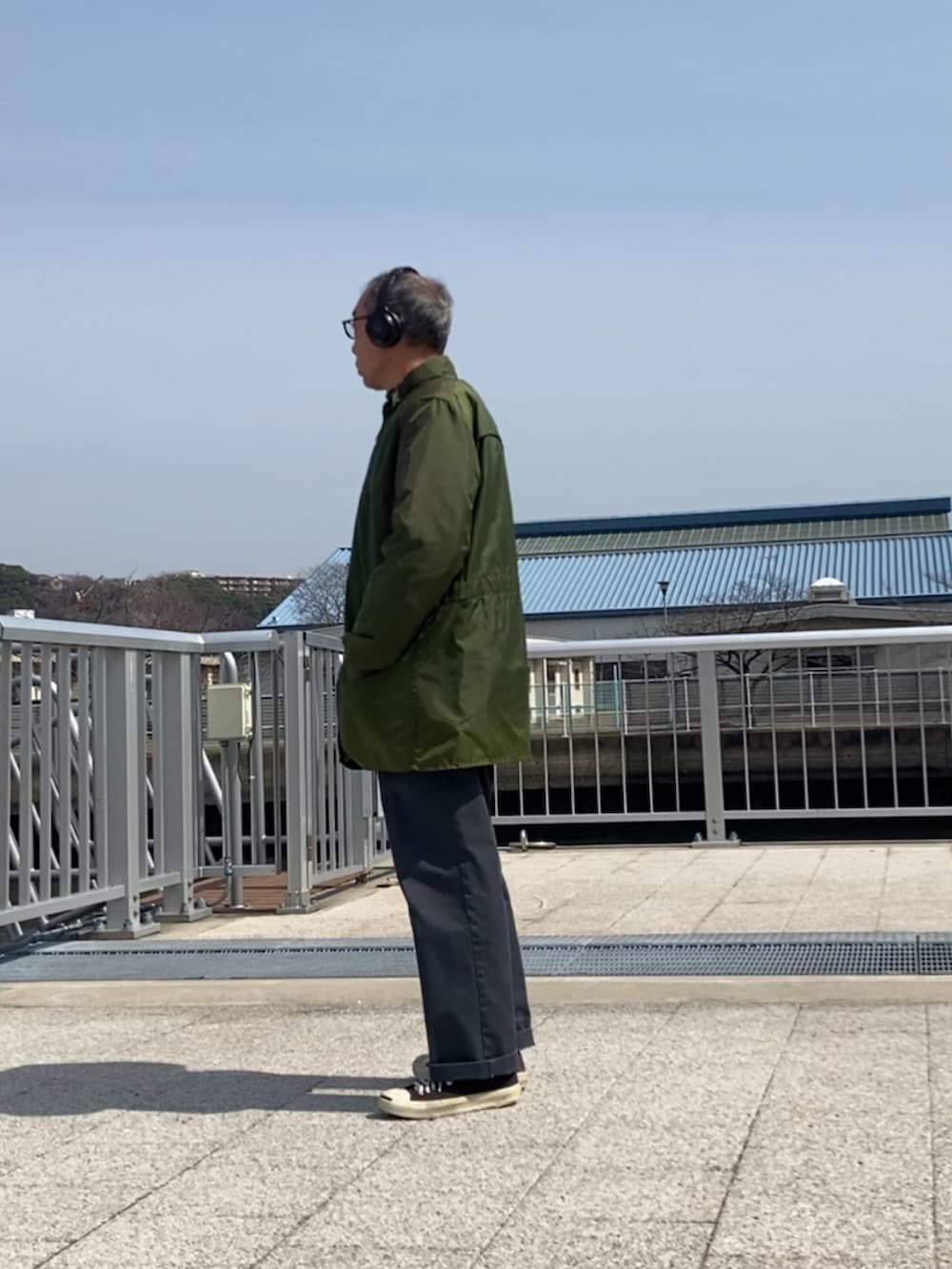 グリーン系のミリタリージャケット、グレー系のチノパンツ、ブラック系のスニーカーを着用したメンズの春コーディネートの2枚目の写真