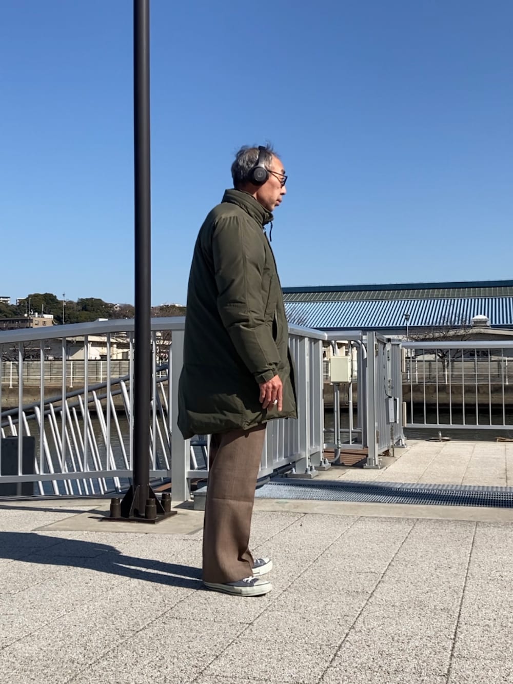 グリーン系のダウンジャケット/コート、ブラウン系のスラックス、ブルー系のスニーカーを着用したメンズの冬コーディネートの2枚目の写真