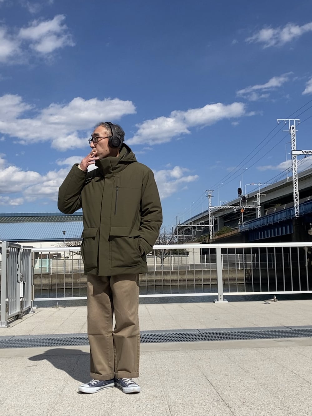 ブラウン系のチノパンツ、グリーン系のダウンジャケット/コート、ブルー系のスニーカーを着用したメンズの春コーディネートの2枚目の写真