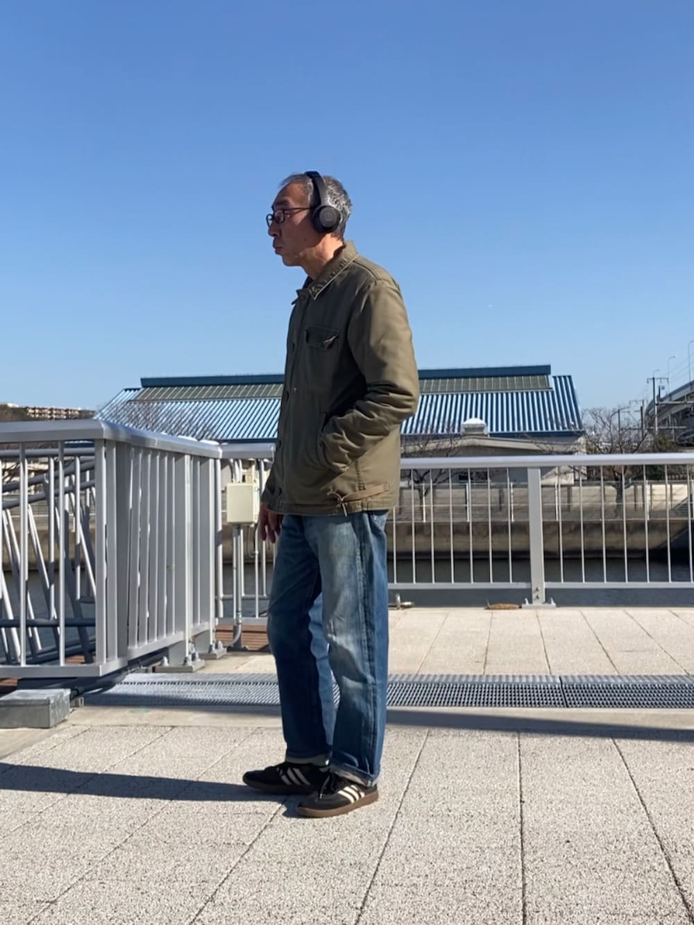 グリーン系のミリタリージャケット、ブルー系のデニムパンツ、ブラック系のスニーカーを着用したメンズの冬コーディネートの2枚目の写真