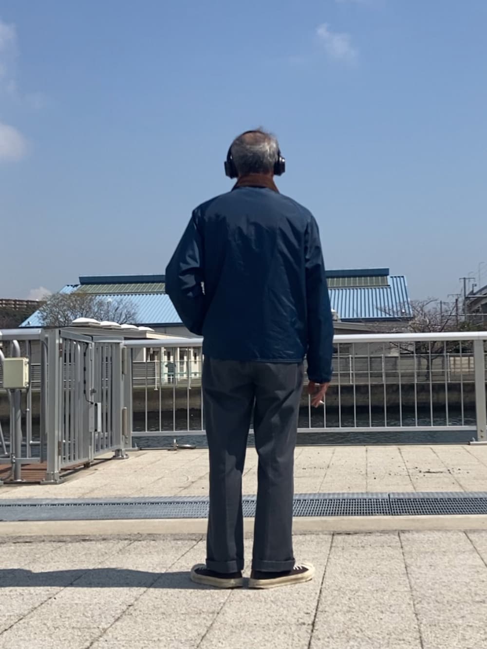 ブルー系のナイロンジャケット、グレー系のチノパンツ、ブラック系のスニーカーを着用したメンズの春コーディネートの3枚目の写真