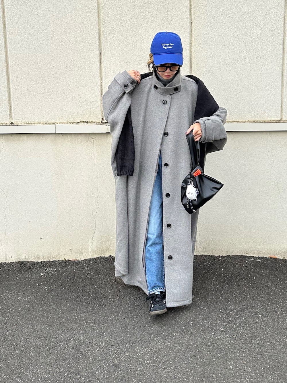 グレー系のステンカラーコート、ブラック系のハンドバッグ、ブルー系のキャップを着用したレディースの冬コーディネートの2枚目の写真