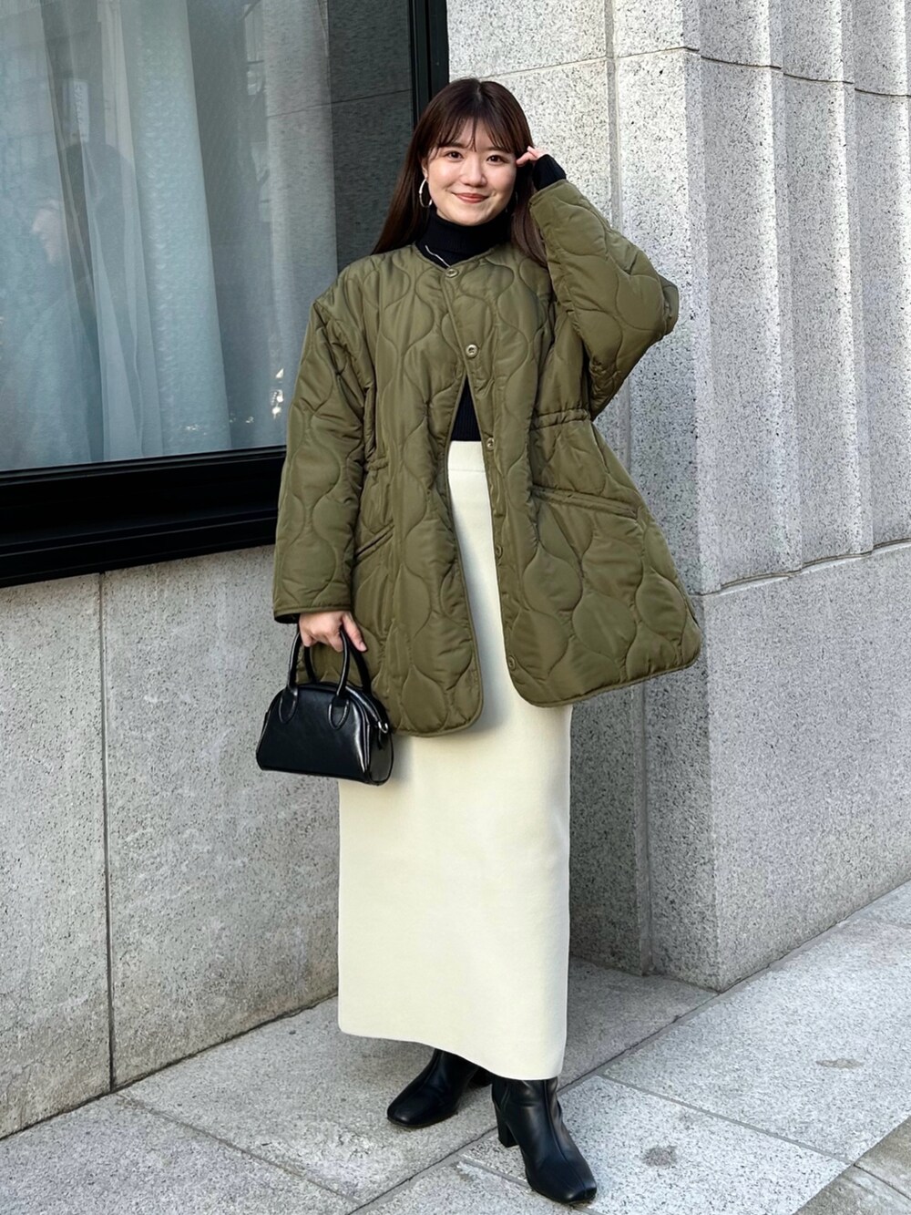 ホワイト系のノーカラーコート、ホワイト系のスカート、ブラウン系のブーツを着用したレディースの冬コーディネートの2枚目の写真