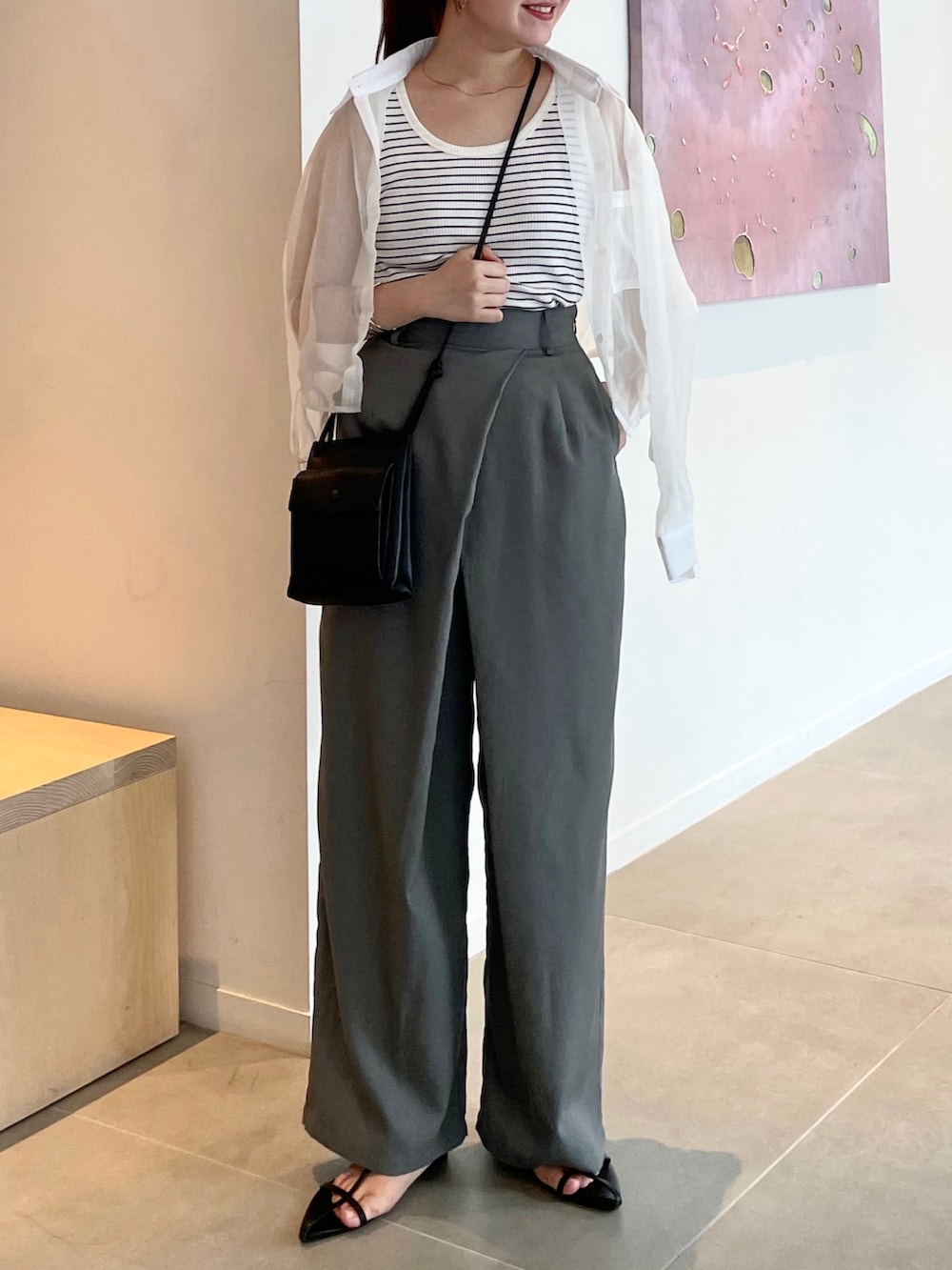 グレー系のスラックス、ホワイト系のサンダル、ブラック系のショルダーバッグを着用したレディースの夏コーディネートの2枚目の写真