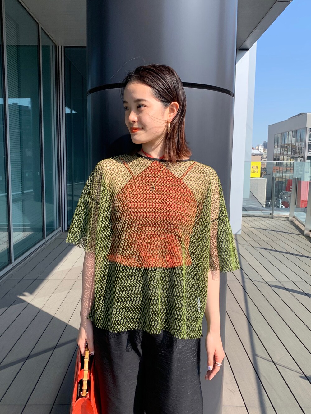 ブラック系のその他パンツ、グリーン系のTシャツ/カットソー、オレンジ系のトートバッグを着用したレディースの春コーディネートの2枚目の写真