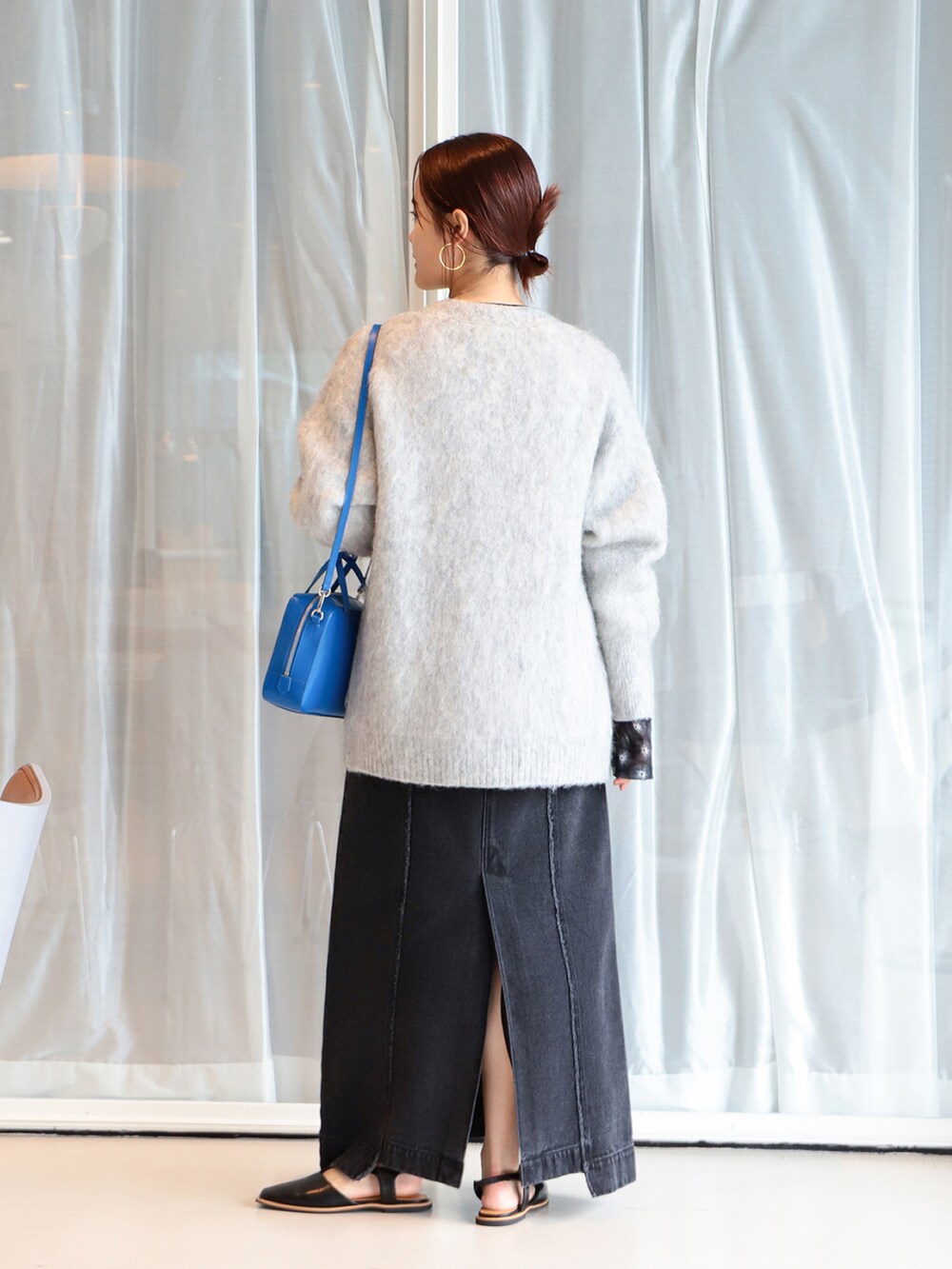 グレー系のニット/セーター、ブラック系のデニムスカート、ブルー系のショルダーバッグを着用したレディースの夏コーディネートの2枚目の写真