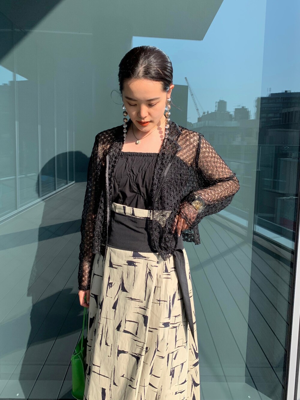 グリーン系のショルダーバッグ、ベージュ系のスカート、ブラック系のその他アウターを着用したレディースの春コーディネートの2枚目の写真