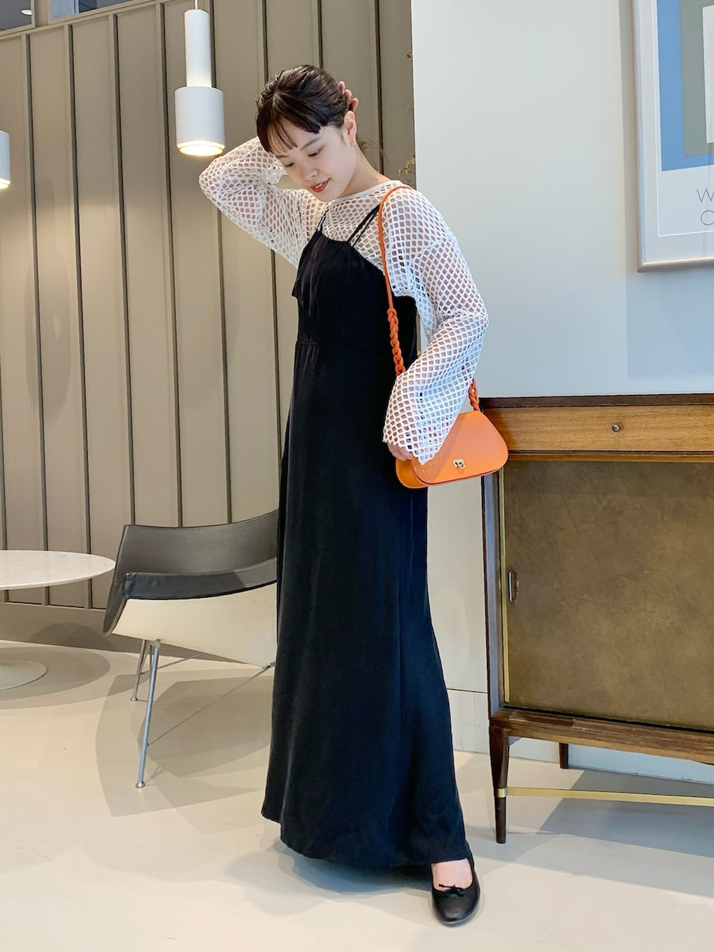 オレンジ系のトートバッグ、ブラック系のワンピース、ホワイト系のTシャツ/カットソーを着用したレディースの春コーディネートの2枚目の写真