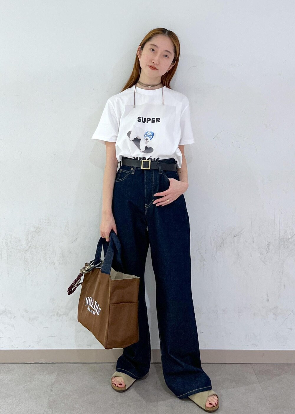 ブラウン系のトートバッグ、ブルー系のデニムパンツ、シルバー系のネックレスを着用したレディースの夏コーディネートの2枚目の写真