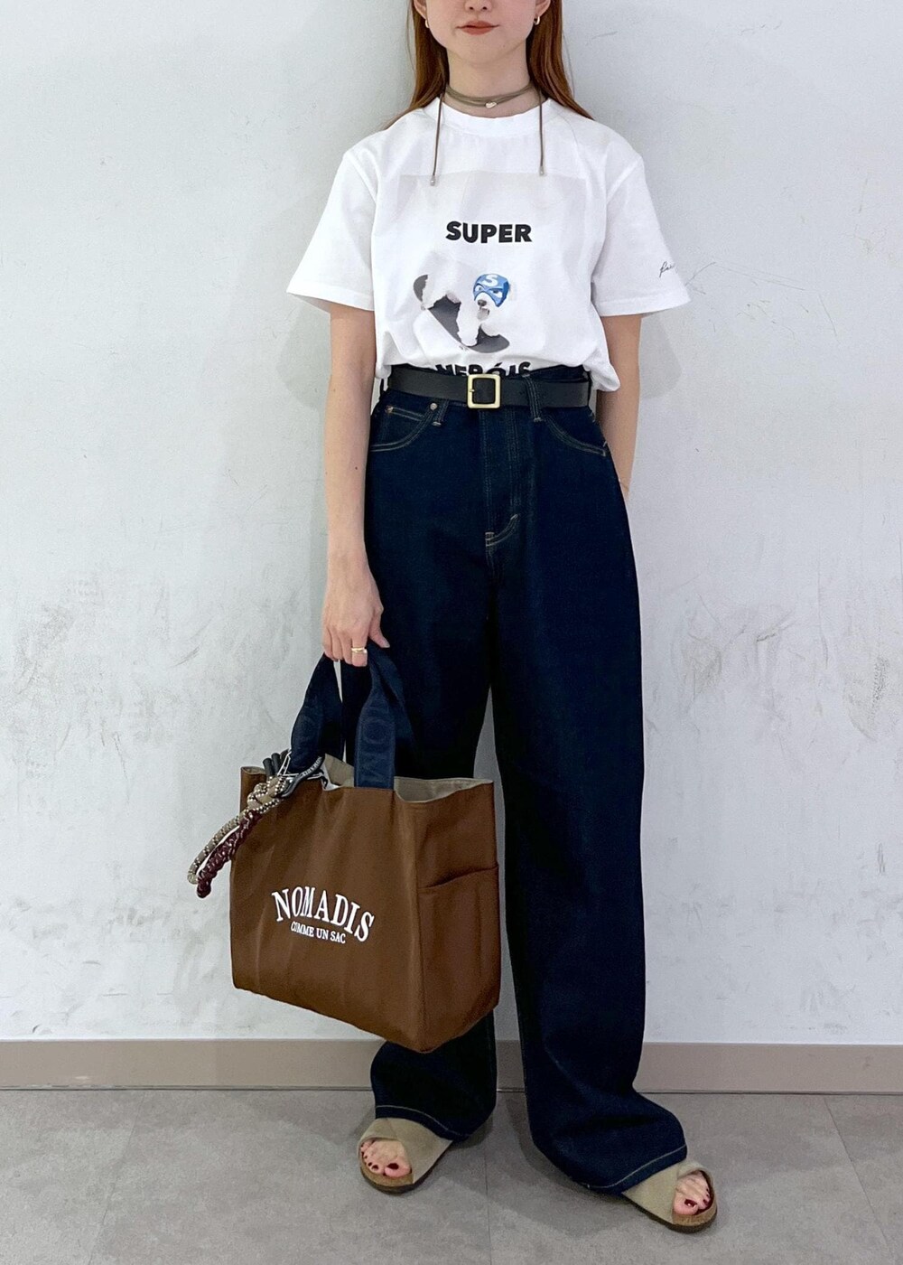 ブラウン系のトートバッグ、ブルー系のデニムパンツ、シルバー系のネックレスを着用したレディースの夏コーディネートの3枚目の写真