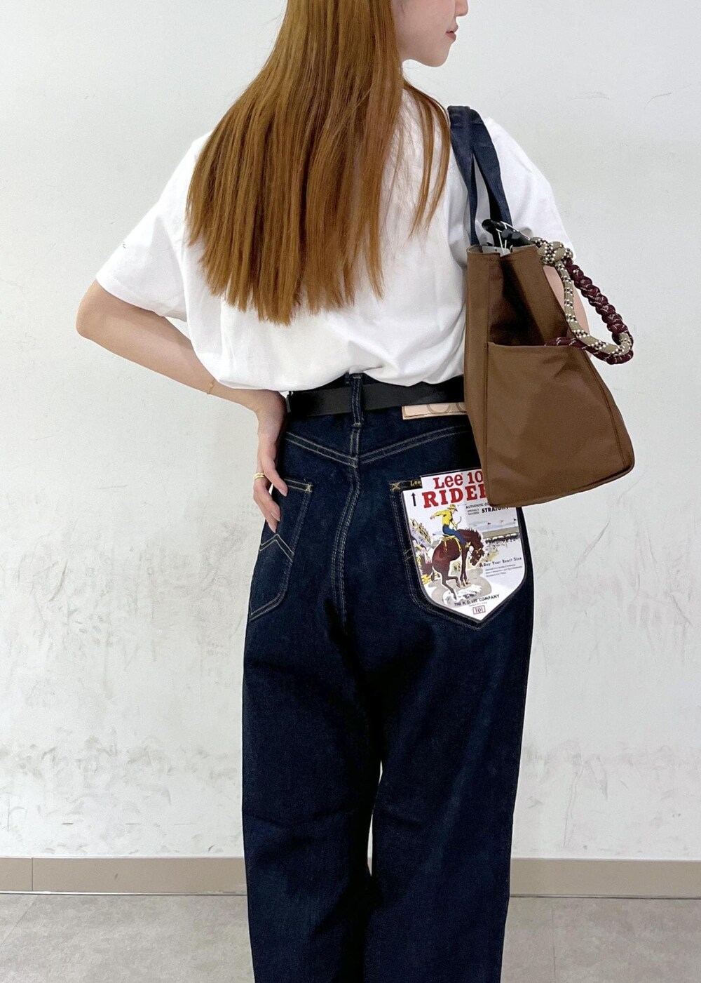 ブラウン系のトートバッグ、ブルー系のデニムパンツ、シルバー系のネックレスを着用したレディースの夏コーディネートの8枚目の写真