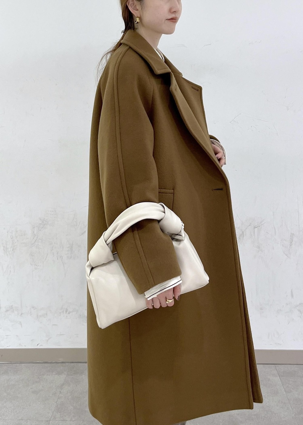 ホワイト系のハンドバッグ、イエロー系のステンカラーコート、ベージュ系のニット/セーターを着用したレディースの秋コーディネートの6枚目の写真