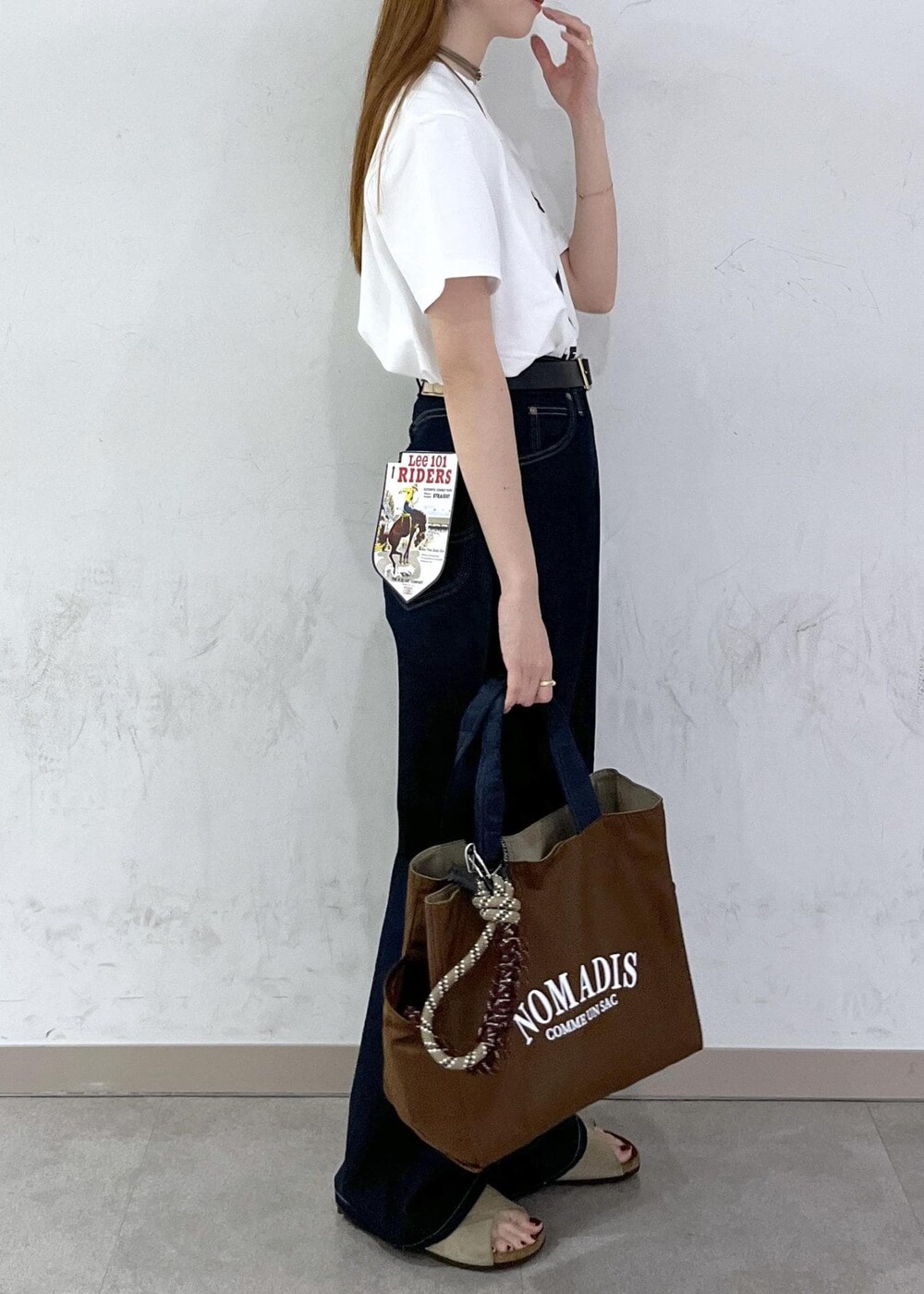 ブラウン系のトートバッグ、ブルー系のデニムパンツ、シルバー系のネックレスを着用したレディースの夏コーディネートの4枚目の写真