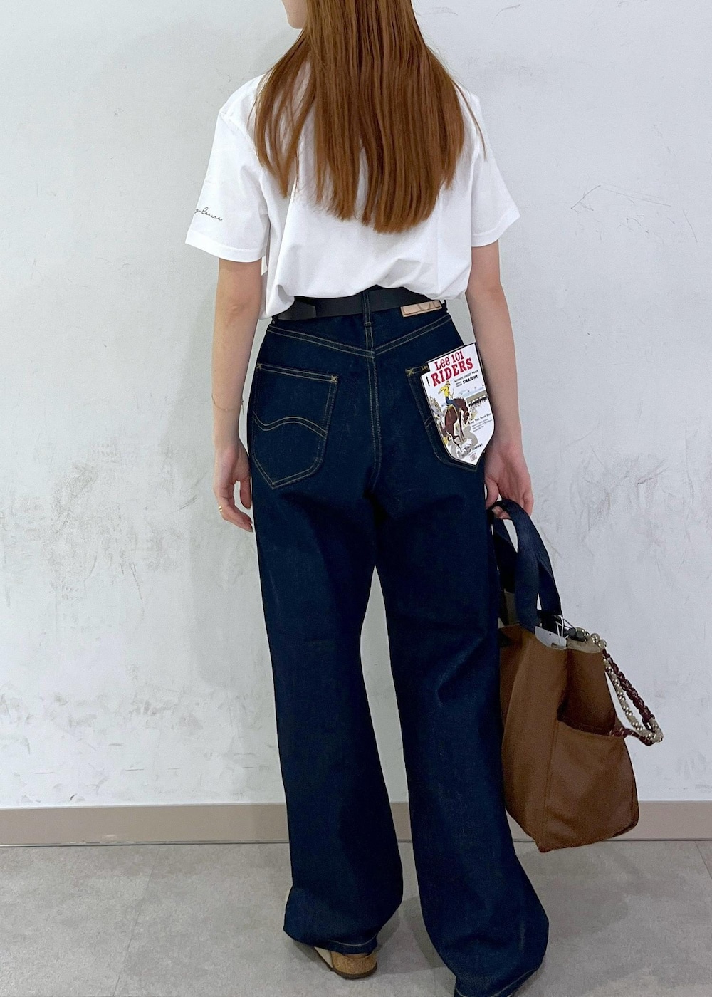 ブラウン系のトートバッグ、ブルー系のデニムパンツ、シルバー系のネックレスを着用したレディースの夏コーディネートの5枚目の写真