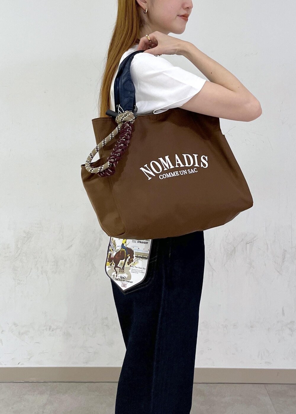 ブラウン系のトートバッグ、ブルー系のデニムパンツ、シルバー系のネックレスを着用したレディースの夏コーディネートの7枚目の写真