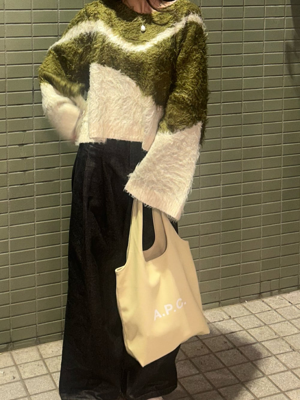 グリーン系のニット/セーター、ベージュ系のトートバッグ、ブラック系のデニムパンツを着用したレディースの秋コーディネートの2枚目の写真