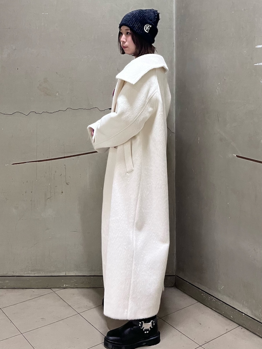 ホワイト系のチェスターコート、レッド系のニット/セーター、ブルー系のデニムパンツを着用したレディースの冬コーディネートの2枚目の写真