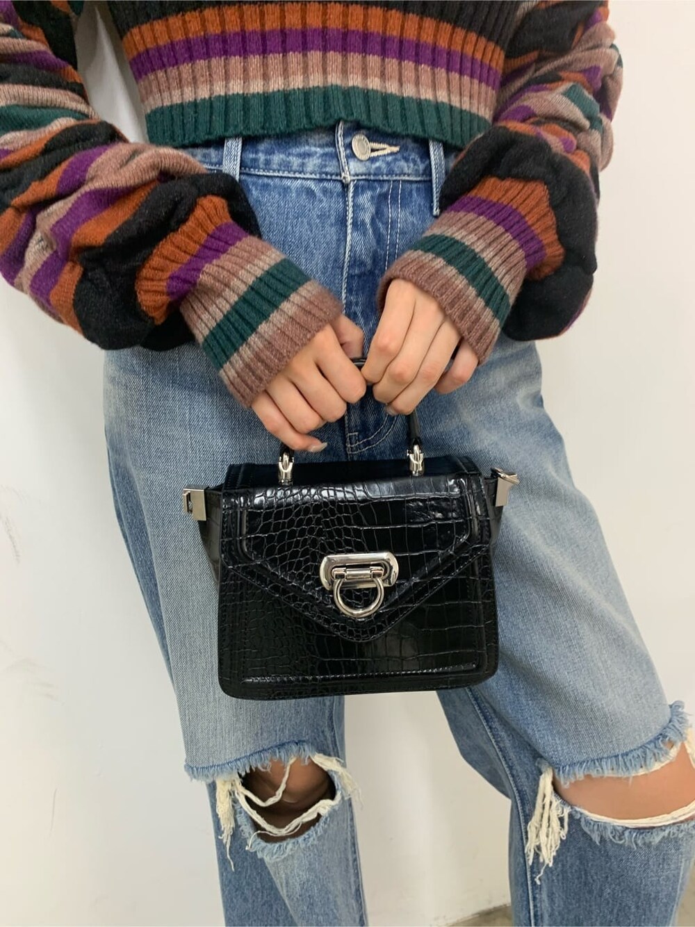 ブラック系のハンドバッグ、ブラック系のブーツ、ブルー系のデニムパンツを着用したレディースの秋コーディネートの8枚目の写真