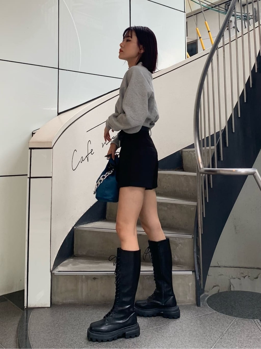 ブラック系のブーツ、ブルー系のハンドバッグ、グレー系のスウェットを着用したレディースの秋コーディネートの2枚目の写真