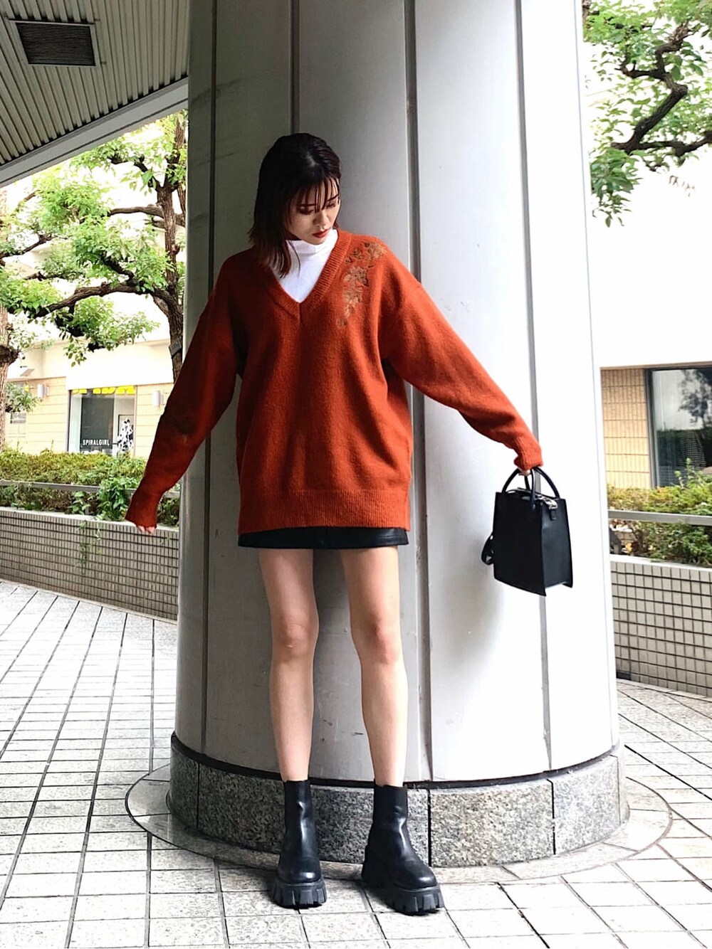 オレンジ系のニット/セーター、ブラック系のブーツ、ブラック系のスカートを着用したレディースの冬コーディネートの2枚目の写真