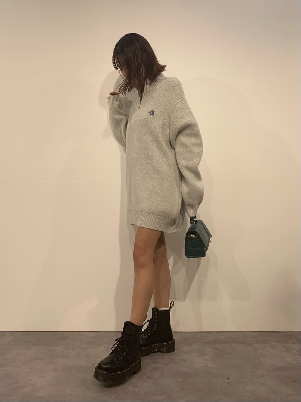 グレー系のニット/セーター、ブラック系のブーツ、グリーン系のショルダーバッグを着用したレディースの秋コーディネートの3枚目の写真