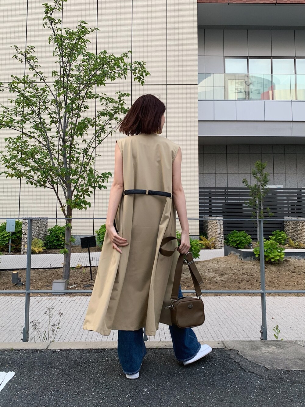 ブルー系のデニムパンツ、ベージュ系のトレンチコート、ブラウン系のタンクトップを着用したレディースの春コーディネートの3枚目の写真