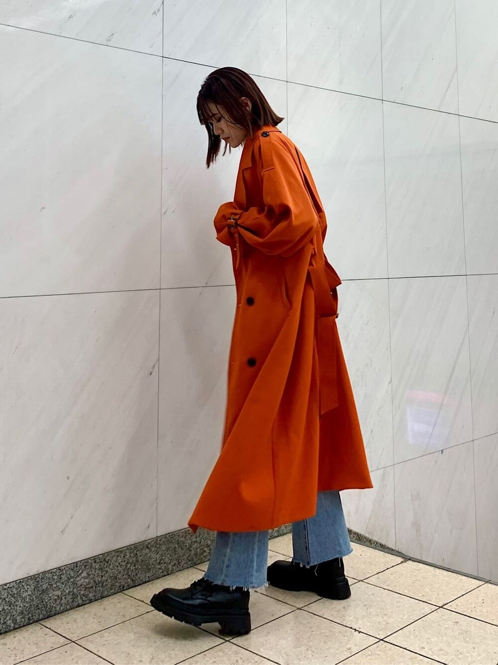 ブラック系のショルダーバッグ、オレンジ系のトレンチコート、ブルー系のデニムパンツを着用したレディースの冬コーディネートの2枚目の写真