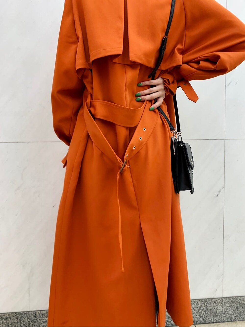 ブラック系のショルダーバッグ、オレンジ系のトレンチコート、ブルー系のデニムパンツを着用したレディースの冬コーディネートの6枚目の写真