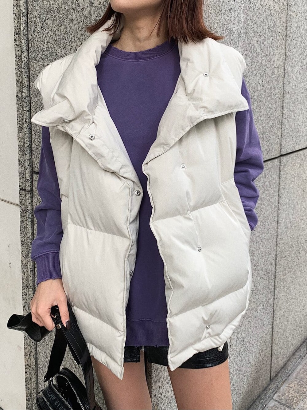 ホワイト系のダウンベスト、パープル系のスウェット、ブラック系のスカートを着用したレディースの秋コーディネートの3枚目の写真
