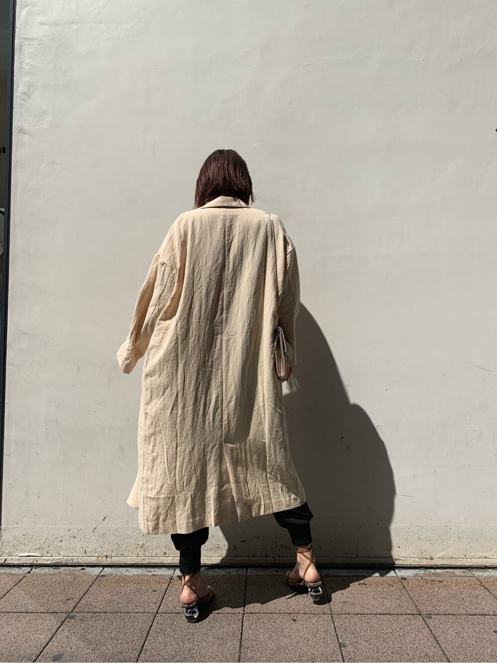 ベージュ系のチェスターコート、ブラック系のその他パンツ、ブラウン系のサンダルを着用したレディースの春コーディネートの2枚目の写真