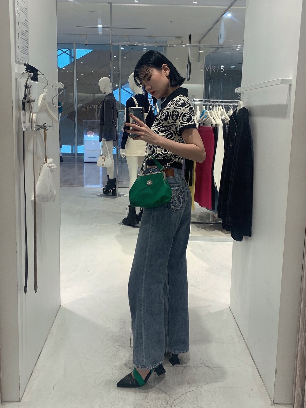 グリーン系のショルダーバッグ、ブルー系のデニムパンツ、ブラック系のニット/セーターを着用したレディースの春コーディネートの2枚目の写真