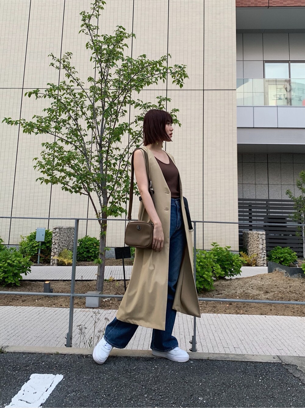 ブルー系のデニムパンツ、ベージュ系のトレンチコート、ブラウン系のタンクトップを着用したレディースの春コーディネートの2枚目の写真
