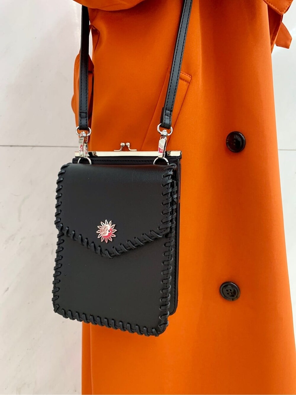 ブラック系のショルダーバッグ、オレンジ系のトレンチコート、ブルー系のデニムパンツを着用したレディースの冬コーディネートの9枚目の写真