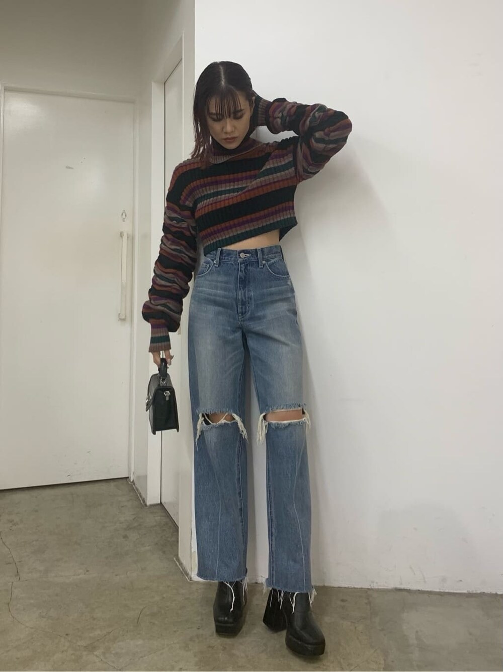 ブラック系のハンドバッグ、ブラック系のブーツ、ブルー系のデニムパンツを着用したレディースの秋コーディネートの2枚目の写真