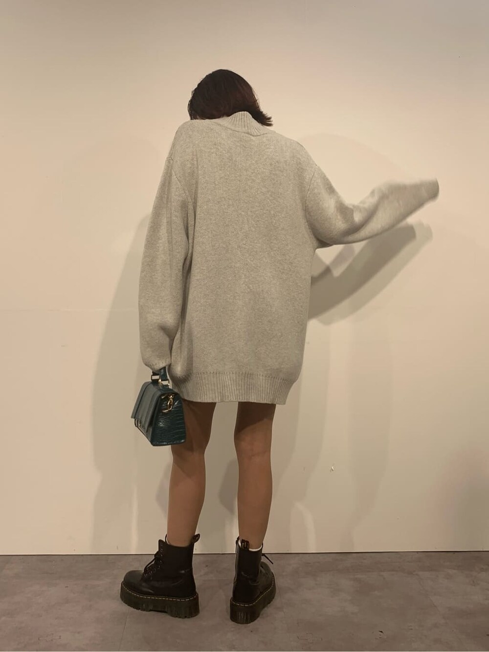 グレー系のニット/セーター、ブラック系のブーツ、グリーン系のショルダーバッグを着用したレディースの秋コーディネートの4枚目の写真