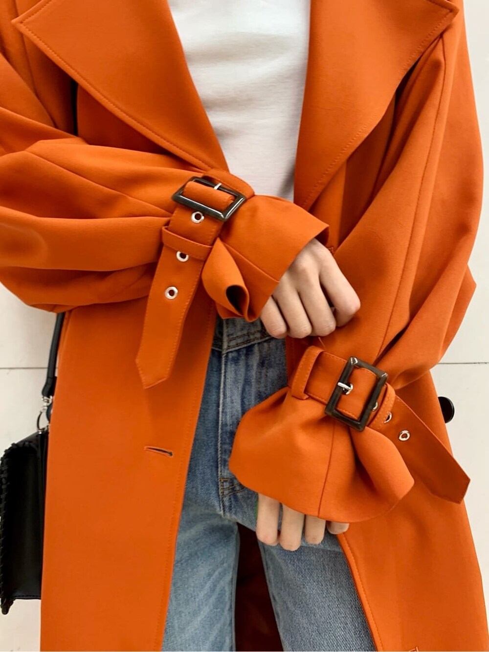 ブラック系のショルダーバッグ、オレンジ系のトレンチコート、ブルー系のデニムパンツを着用したレディースの冬コーディネートの7枚目の写真