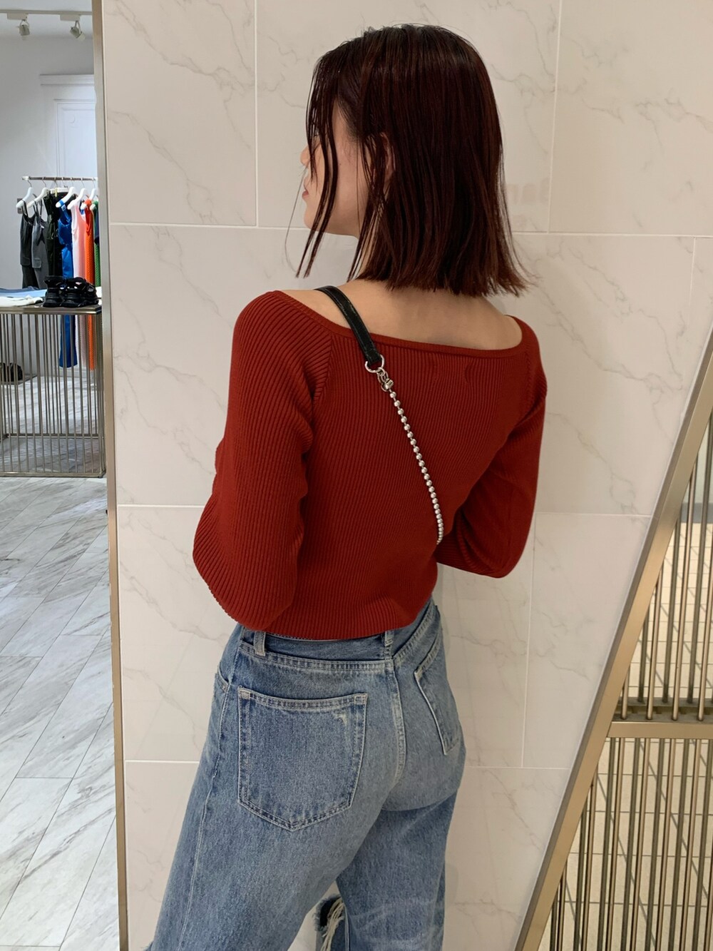 レッド系のニット/セーター、ブラック系のショルダーバッグ、ブルー系のデニムパンツを着用したレディースの夏コーディネートの4枚目の写真