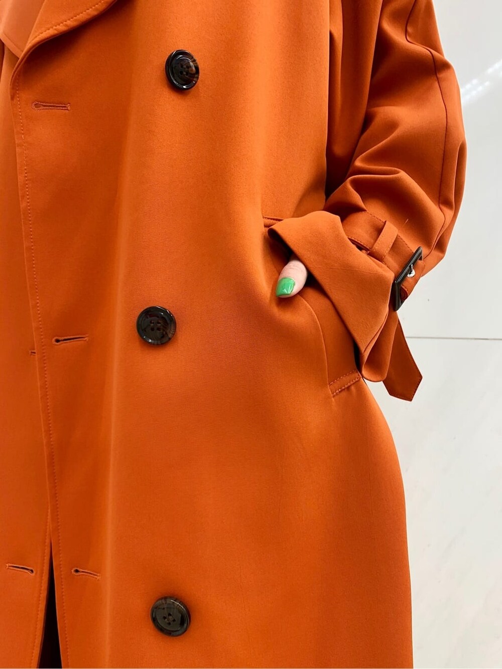 ブラック系のショルダーバッグ、オレンジ系のトレンチコート、ブルー系のデニムパンツを着用したレディースの冬コーディネートの5枚目の写真