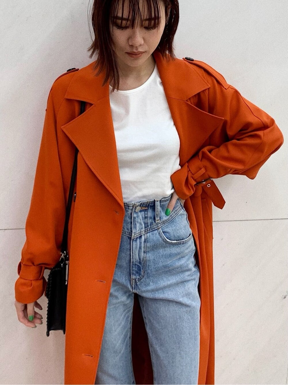 ブラック系のショルダーバッグ、オレンジ系のトレンチコート、ブルー系のデニムパンツを着用したレディースの冬コーディネートの4枚目の写真