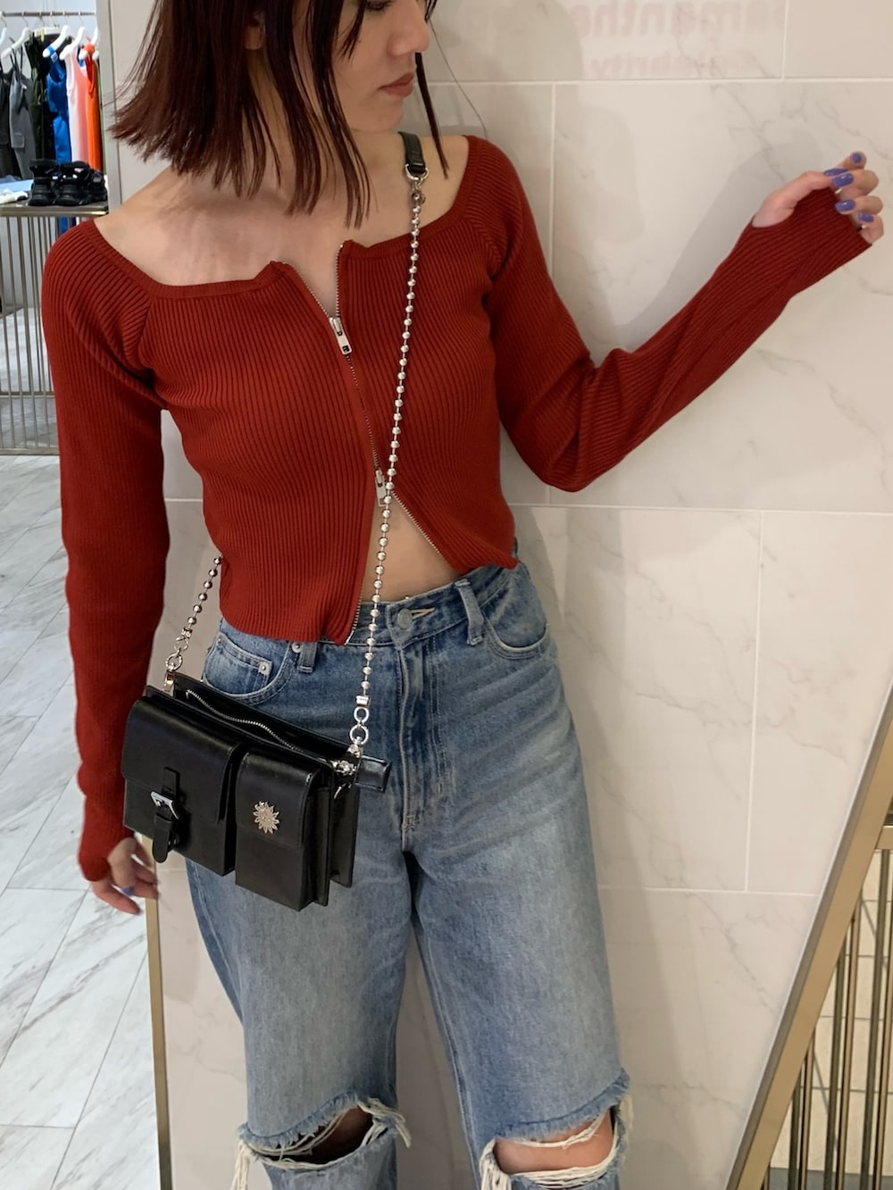 レッド系のニット/セーター、ブラック系のショルダーバッグ、ブルー系のデニムパンツを着用したレディースの夏コーディネートの3枚目の写真