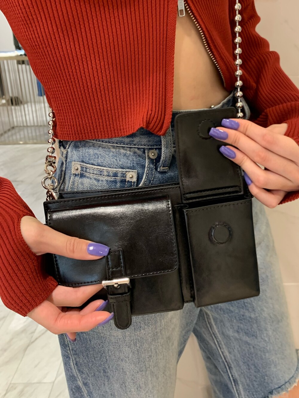 レッド系のニット/セーター、ブラック系のショルダーバッグ、ブルー系のデニムパンツを着用したレディースの夏コーディネートの7枚目の写真