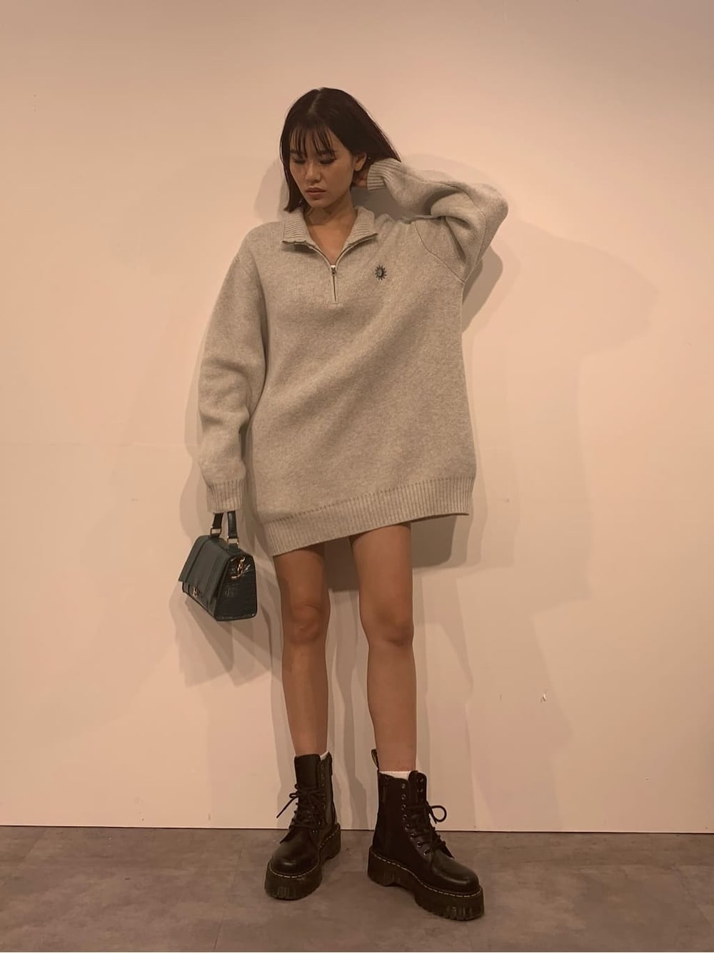 グレー系のニット/セーター、ブラック系のブーツ、グリーン系のショルダーバッグを着用したレディースの秋コーディネートの2枚目の写真