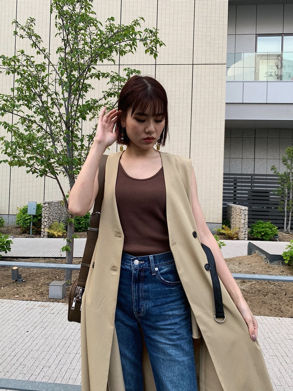 ブルー系のデニムパンツ、ベージュ系のトレンチコート、ブラウン系のタンクトップを着用したレディースの春コーディネートの6枚目の写真
