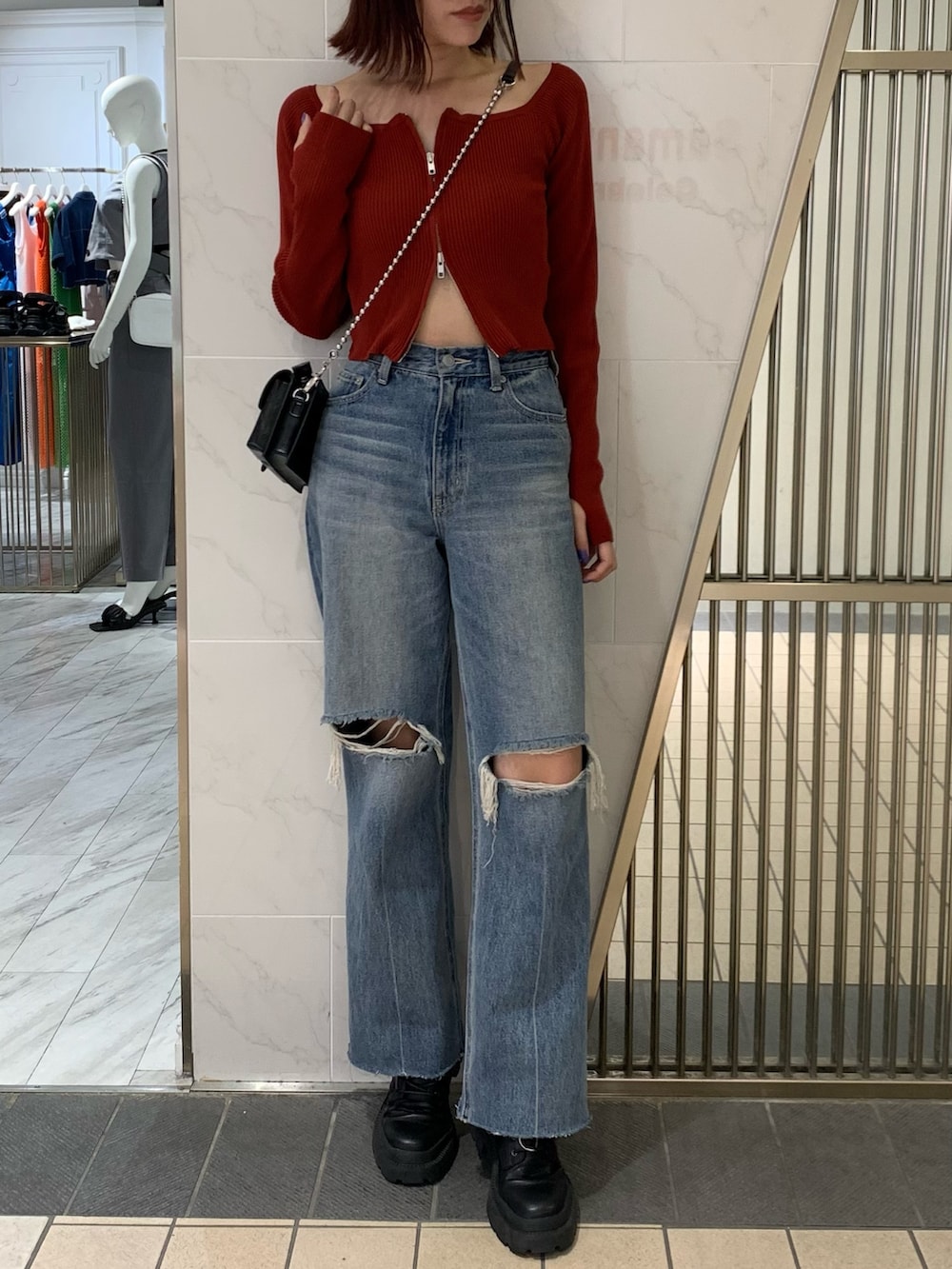 レッド系のニット/セーター、ブラック系のショルダーバッグ、ブルー系のデニムパンツを着用したレディースの夏コーディネートの2枚目の写真