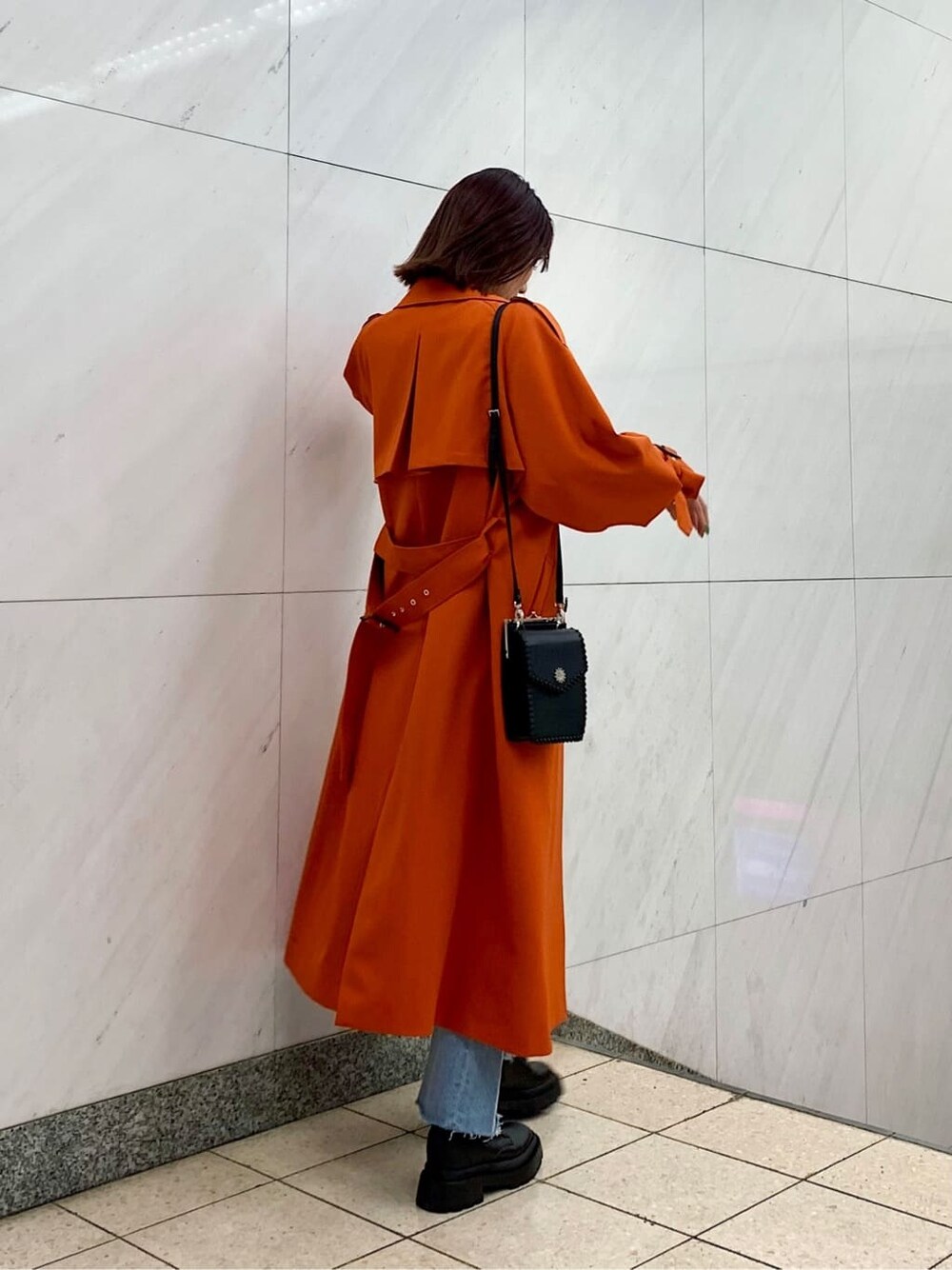 ブラック系のショルダーバッグ、オレンジ系のトレンチコート、ブルー系のデニムパンツを着用したレディースの冬コーディネートの3枚目の写真
