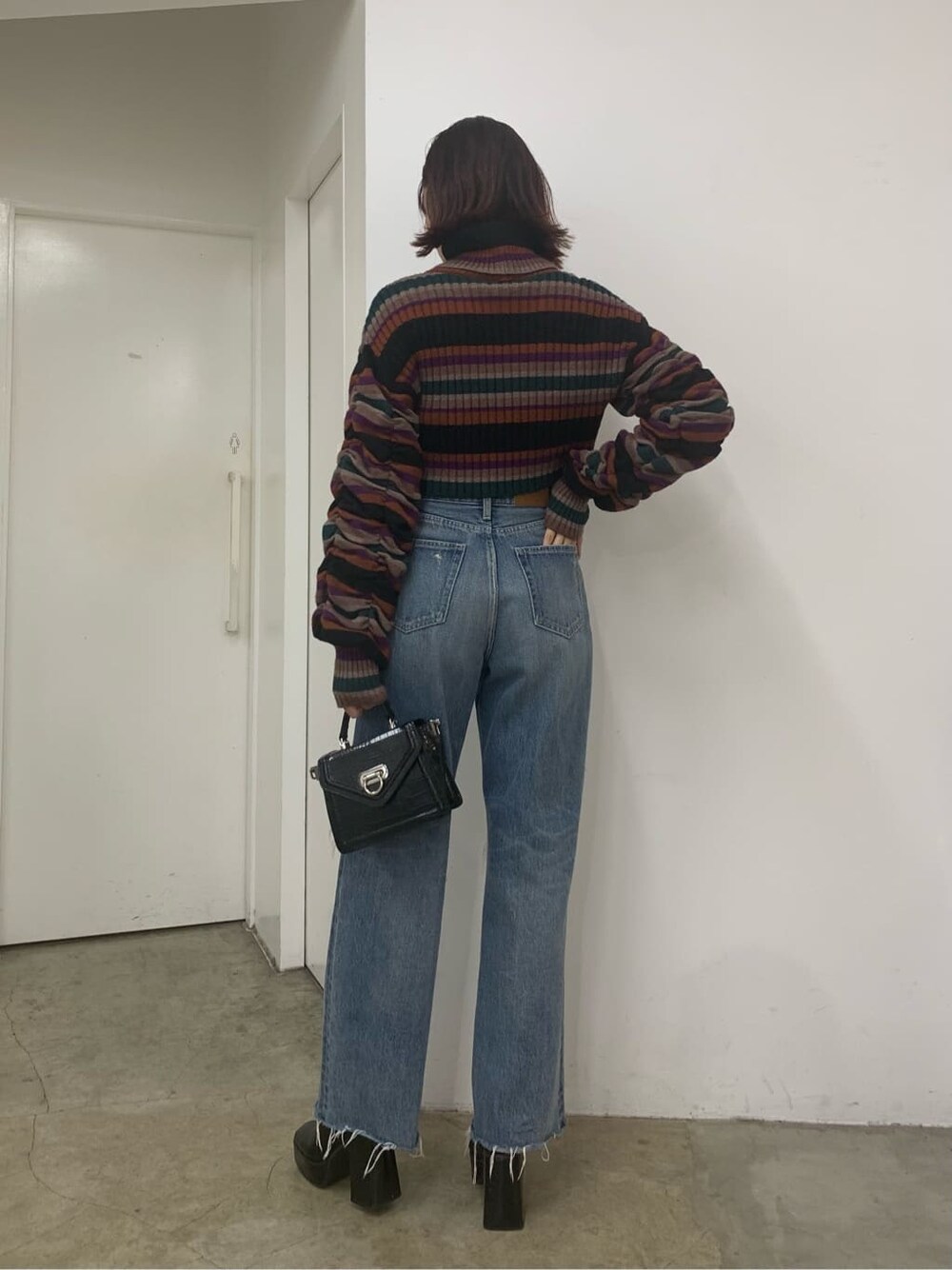 ブラック系のハンドバッグ、ブラック系のブーツ、ブルー系のデニムパンツを着用したレディースの秋コーディネートの4枚目の写真