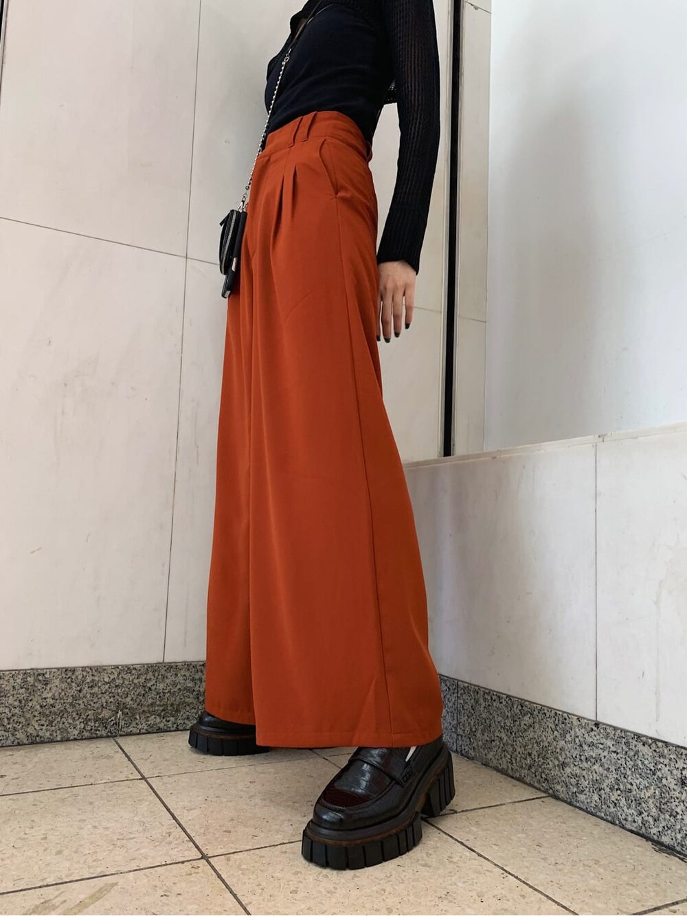 オレンジ系のその他パンツ、ブラック系のローファー、ブラック系のスマホケース/カバーを着用したレディースの秋コーディネートの3枚目の写真