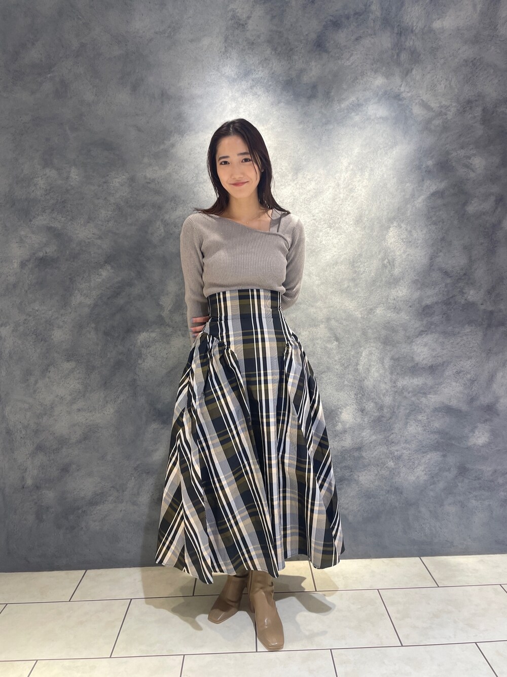 グレー系のニット/セーター、ベージュ系のブーツ、オレンジ系のスカートを着用したレディースの秋コーディネートの2枚目の写真