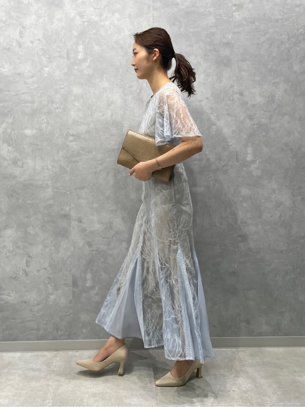 ゴールド系のクラッチバッグ、ベージュ系のパンプス、ブルー系のドレスを着用したレディースの春コーディネートの4枚目の写真