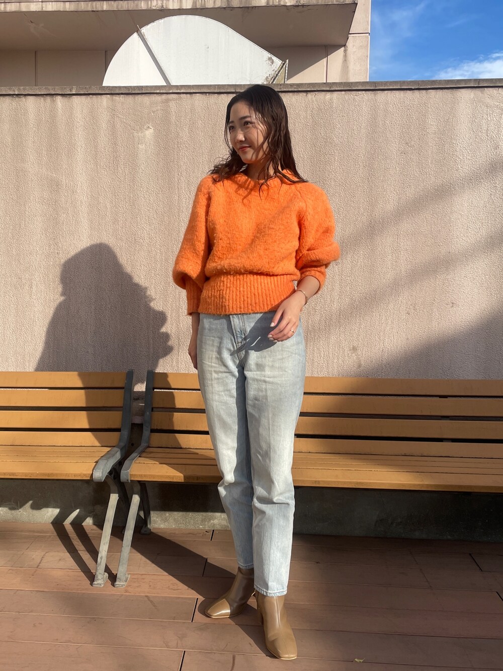 ブルー系のデニムパンツ、オレンジ系のニット/セーター、ベージュ系のブーツを着用したレディースの冬コーディネートの2枚目の写真
